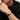 Man wearing a black braided bracelet with a gold-tone engraved clasp