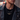 Man in a black leather jacket wearing a layered black cord necklace with bead pendant