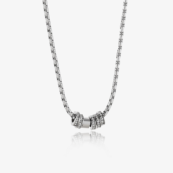 collar de cadena plateada con tres anillos apilados como colgante, dos con piedras transparentes, sobre fondo claro