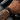 Man wearing a black braided leather bracelet with a gold-tone engraved plate on his wrist