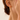 Close-up of a gold-tone large hoop earring worn on an ear, hand touching the cheek