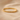 Detalle de pulsera rígida dorada de rombos sobre fondo beige